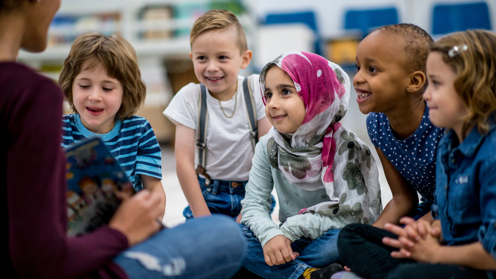 Students sitting on a carpet reading with an educator